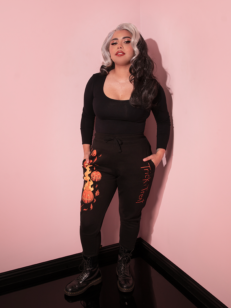 Model tucking her hands into the side pockets on the TRICK R TREAT™ Jack O' Lantern Sweatpants from retro clothing brand Vixen Clothing.