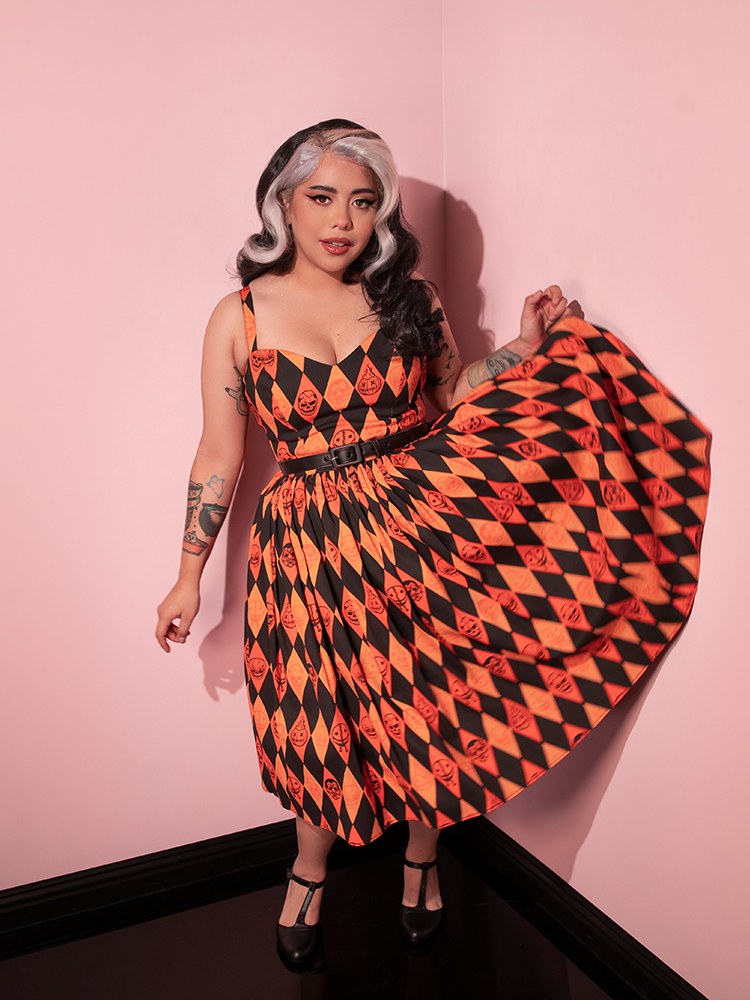 Model flips the skrit section of the TRICK R TREAT™ Sweetheart Swing Dress in Halloween Harlequin Print up high to show off the spooky print.