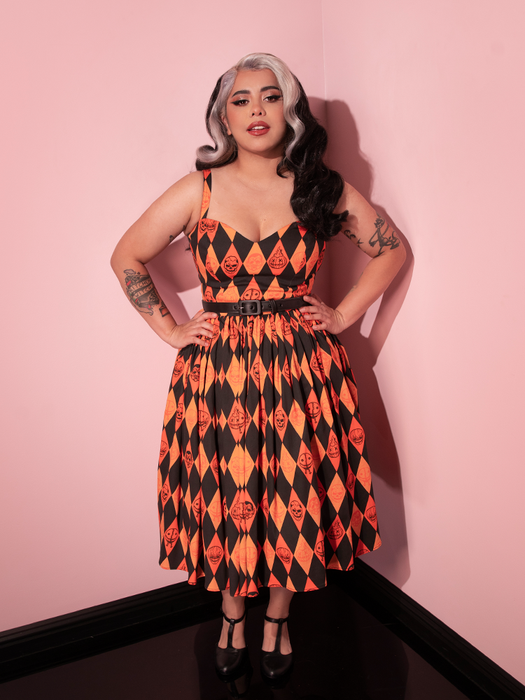 Silver and black haired model posing with her hands on her hips wearing the TRICK R TREAT™ Sweetheart Swing Dress in Halloween Harlequin Print.