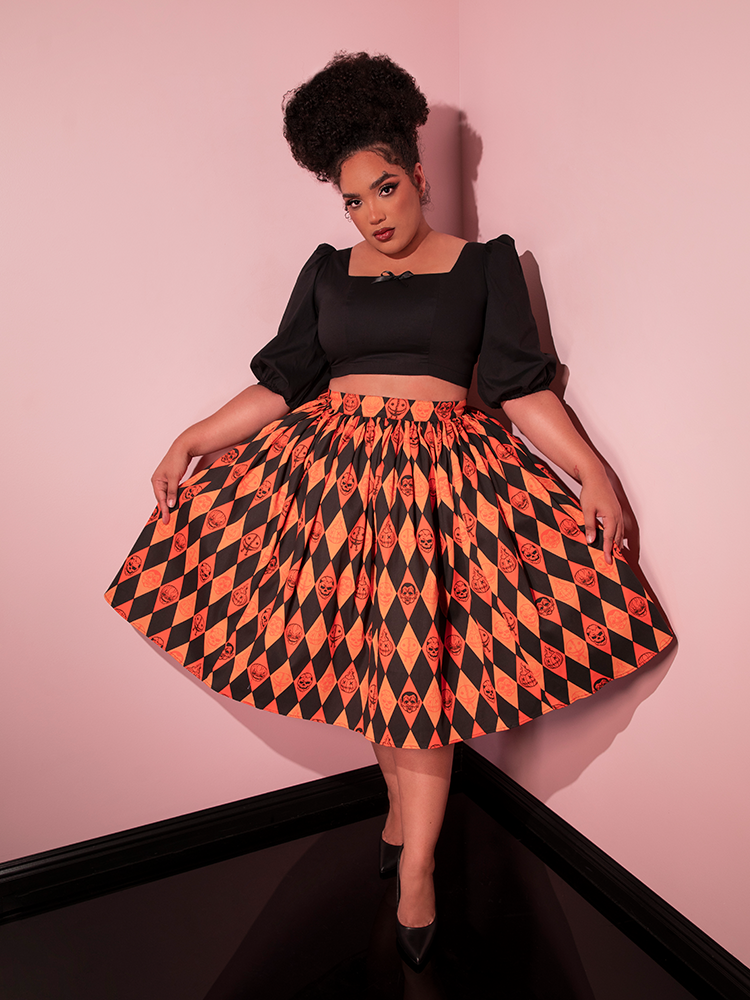 Model holding out the sides of the TRICK R TREAT™ Swing Skirt in Halloween Harlequin Print to show the intricately spooky print on the retro skirt.