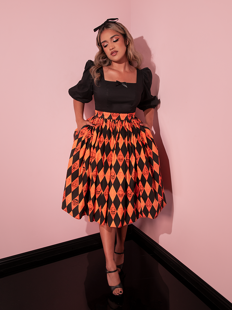 Model tucks her hands into the pockets of the TRICK R TREAT™ Swing Skirt in Halloween Harlequin Print while wistfully looking away. 