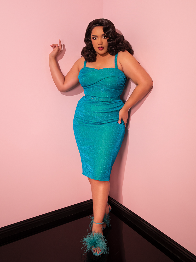 A vision of beauty unfolds in the Jawbreaker Wiggle Dress in Turquoise Lurex, as modeled by a striking woman in Vixen Clothing's retro line.