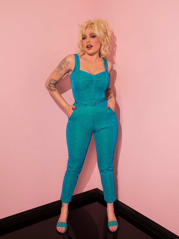 The stunning model effortlessly captures attention in a playful and seductive stance, adorned in the Turquoise Lurex Cigarette Pants from Vixen Clothing's retro collection.