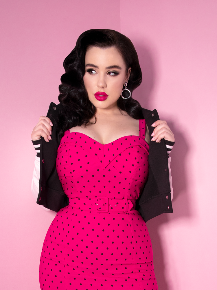 Rachel Sedory pulling back her Vixen Girl Gang Letterman Jacket to reveal the bright pink retro style dress underneath.