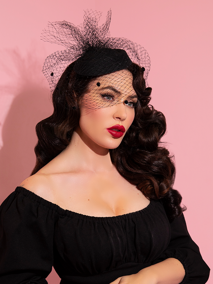 Micheline Pitt gazes off camera while modeling the latest retro style clothing accessory from Vixen Clothing - the Vintage Style Pillbox Hat With Veil from Vixen Clothing.