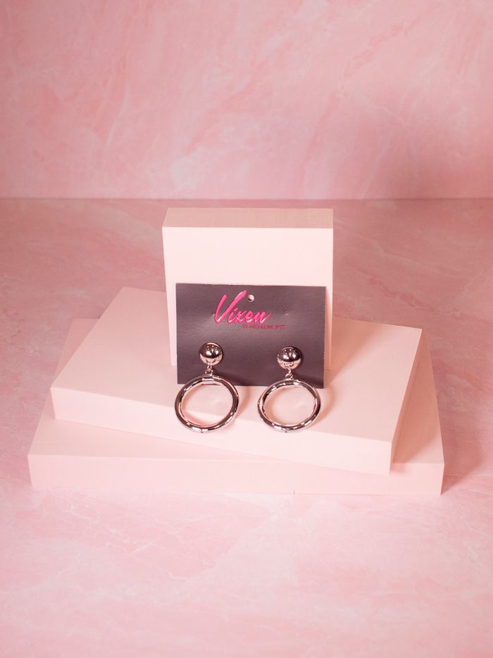 Product shot of the Bad Girl Hoop Earrings in Silver shot on a pink background - item available from retro clothing brand Vixen Clothing.