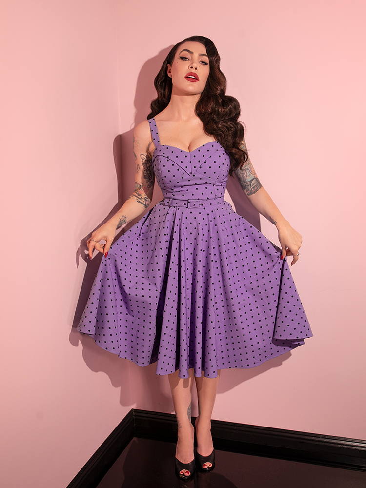 In a delightful showcase of retro chic, Micheline Pitt playfully poses in the Sunset Purple Polka Dot Maneater Swing Dress by Vixen Clothing.