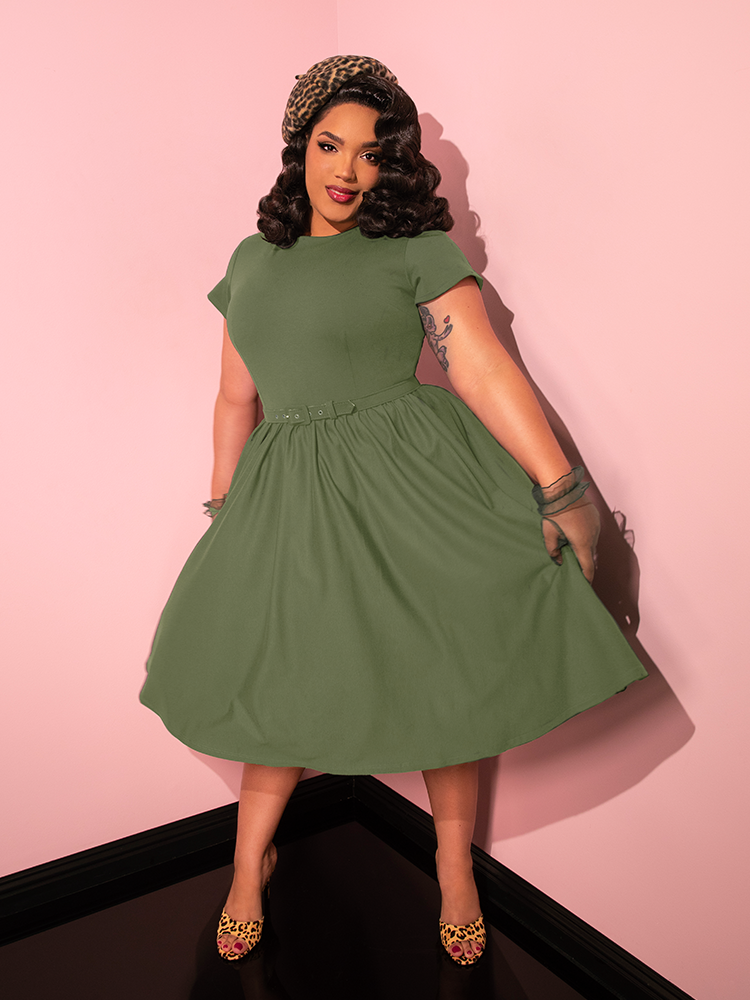 With grace and poise, the female model flaunts the Avon Swing Dress in Sage Green by Vixen Clothing, striking a series of captivating poses.