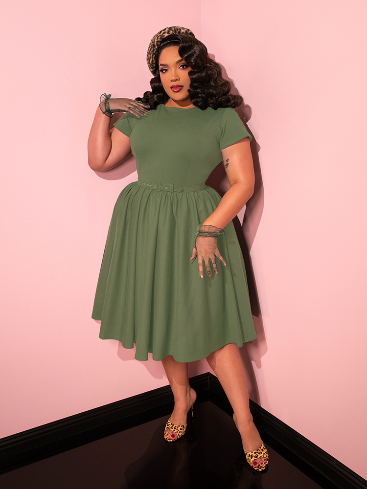 Mesmerizing in every stance, the female model brings life to the Avon Swing Dress in Sage Green from Vixen Clothing's vintage-inspired collection.
