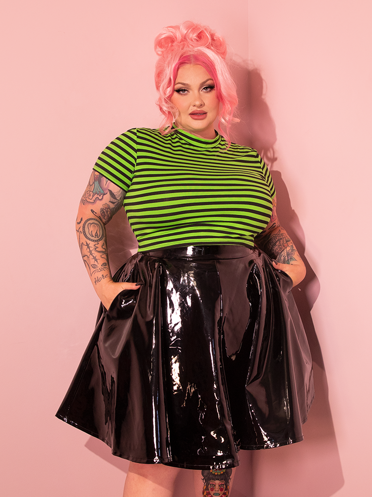 Posing effortlessly, pink-haired female model dons the Bad Girl Crop Top in Slime Green and Black Stripes, a standout piece from Vixen Clothing's retro collection.