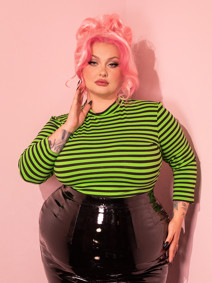 A stunning female model dons the Bad Girl 3/4 Sleeve Top in Striking Slime Green and Black Stripes by the retro clothing brand Vixen Clothing.
