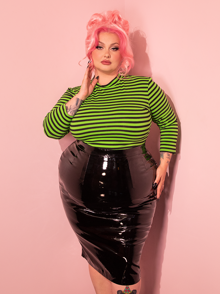 Step into the world of fashion with a gorgeous female model wearing the Bad Girl 3/4 Sleeve Top in Eye-catching Slime Green and Black Stripes, courtesy of Vixen Clothing's retro collection.
