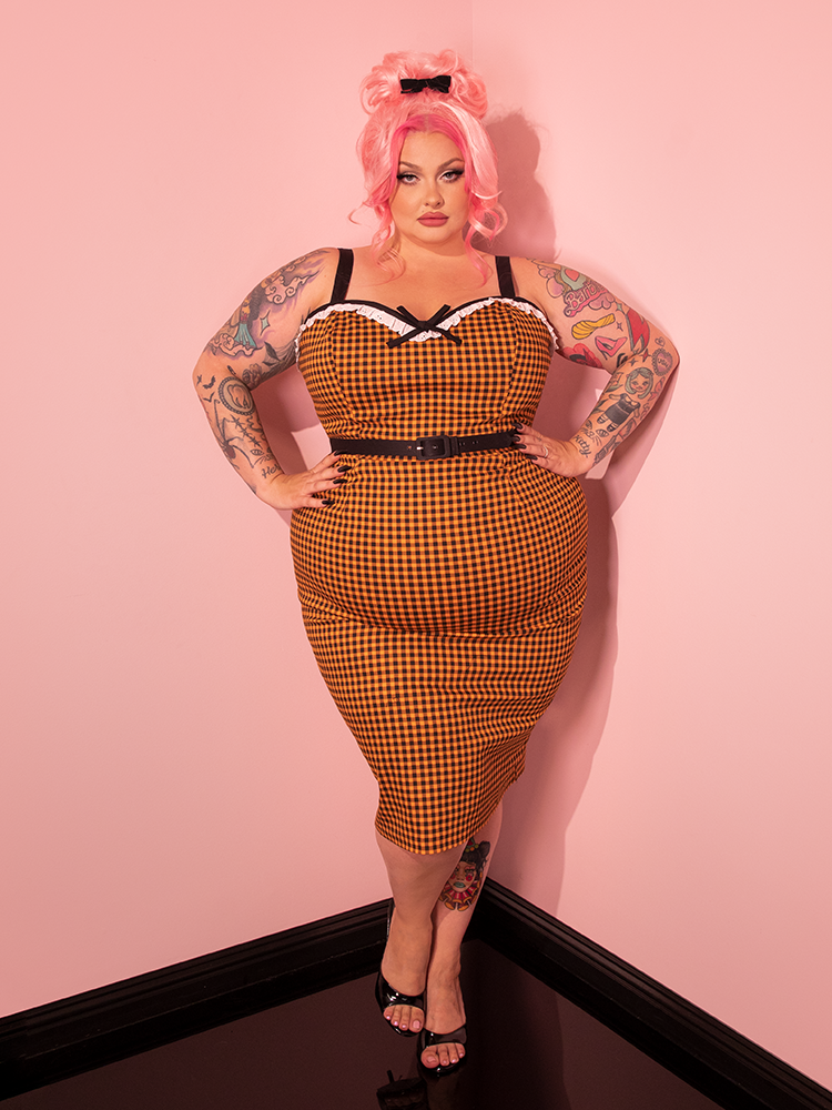 Experience the nostalgia of the past with our beautiful retro-era model showcasing the Bardot Beauty Wiggle Dress in Orange Gingham, expertly crafted by Vixen Clothing, the vintage clothing and retro dress brand.