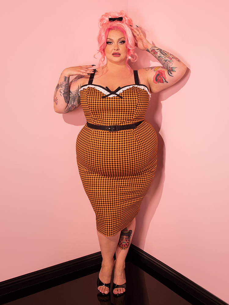 Reveal the timeless elegance of retro fashion as our gorgeous retro-era model graces the scene in the Bardot Beauty Wiggle Dress, adorned with Orange Gingham from Vixen Clothing, the trusted vintage clothing and retro dress brand.