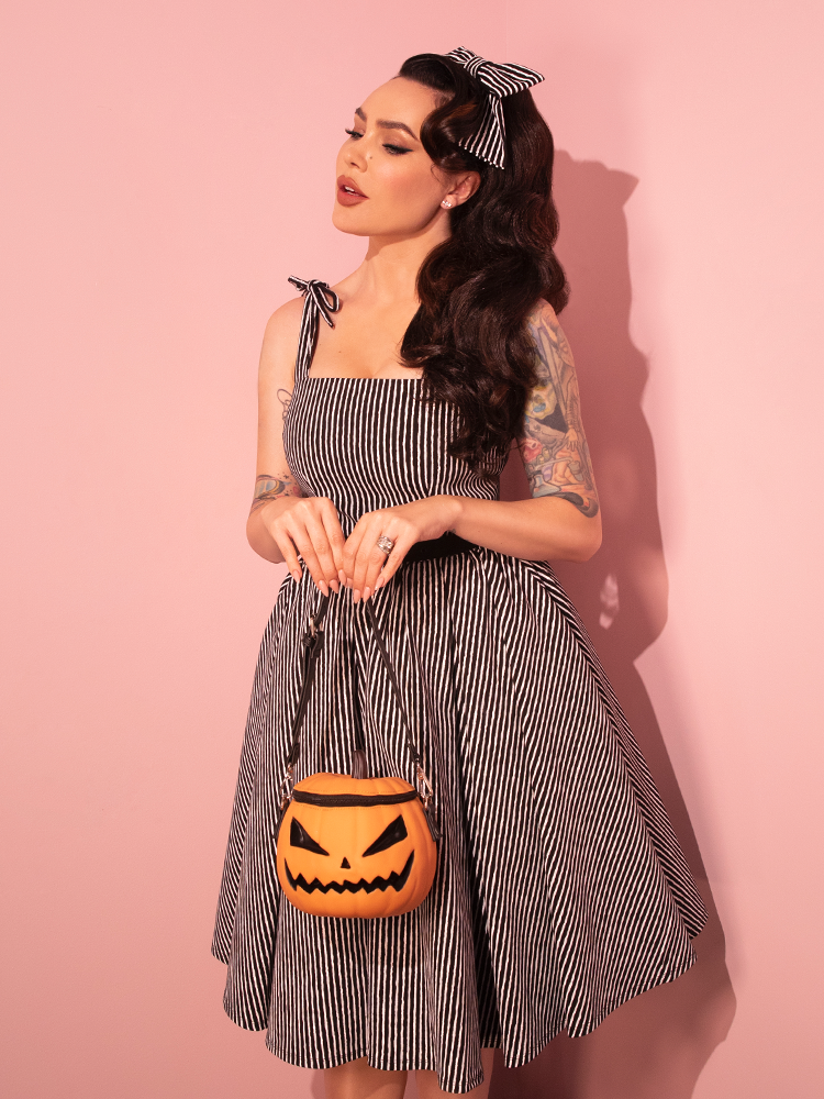 Witness the beauty of our female model as she proudly showcases the Dream House Swing Dress and Matching Hair Bow in Halloween Thin Black and White Stripes from Vixen Clothing, the leading brand in retro dress and vintage attire.