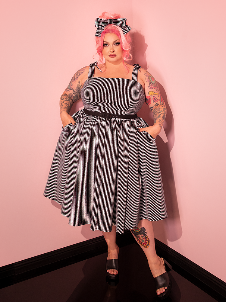 Discover the brand new Dream House Swing Dress and Matching Hair Bow in Captivating Halloween Thin Black and White Stripes by Vixen Clothing, as our stunning female model beautifully showcases the blend of retro charm and modern style.