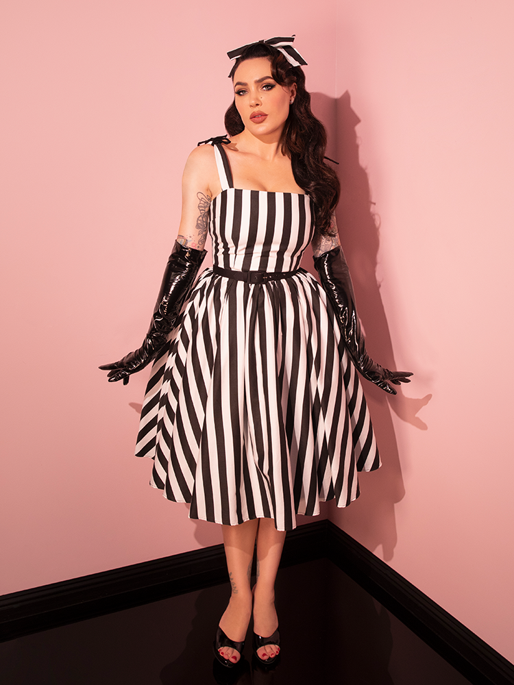Revisit the retro era with a female model showcasing the Dream House Swing Dress and Matching Hair Bow, featuring classic Black and White Stripes by Vixen Clothing.