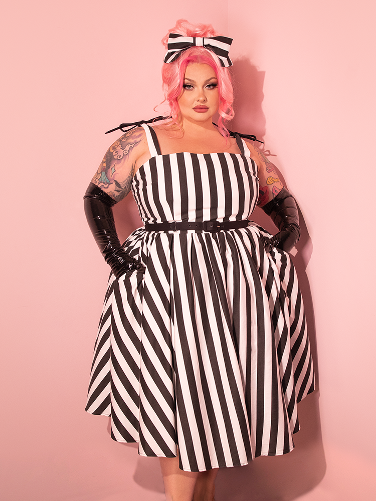 In the retro era, a female model showcases the Dream House Swing Dress and Matching Hair Bow in Bold Black and White Stripes, crafted by the vintage and retro dressmaker Vixen Clothing.
