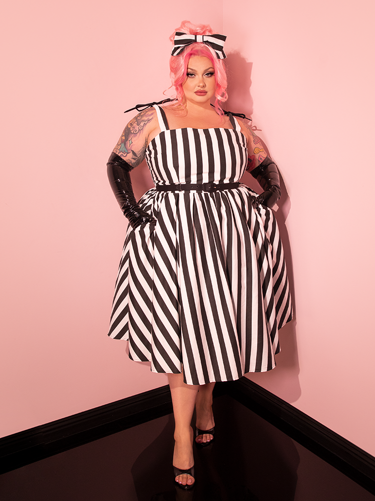 Step back in time with a female model channeling retro vibes in the Dream House Swing Dress and Matching Hair Bow, featuring Thick Black and White Stripes by Vixen Clothing.