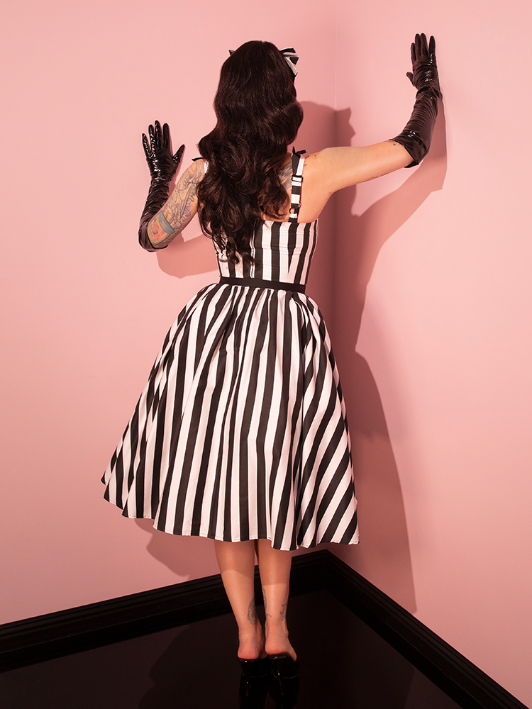 Embark on a journey through time with a female model elegantly wearing the Dream House Swing Dress and Matching Hair Bow in Striking Black and White Stripes, courtesy of Vixen Clothing's retro design.