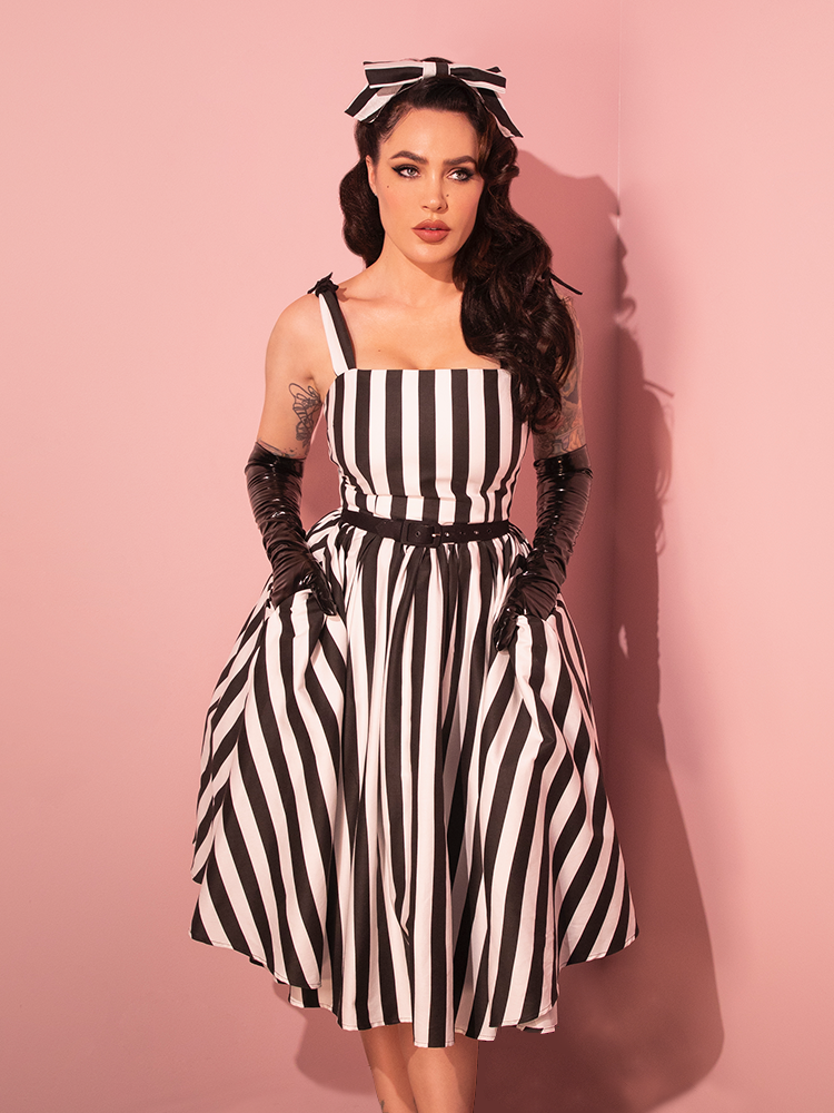 Take a trip down memory lane with a female model adorned in the Dream House Swing Dress and Matching Hair Bow, graced with Thick Black and White Stripes from Vixen Clothing's retro collection.