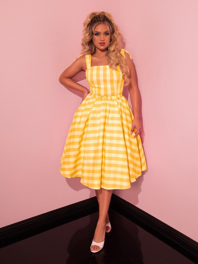 Showcasing sophistication, the beautiful model wears Vixen Clothing's Dream-House Swing Dress and Matching Bow in Yellow Gingham, epitomizing retro chic.