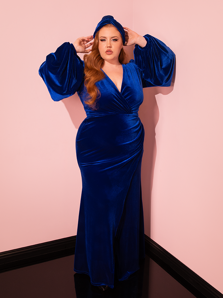 Red-haired female model is a vision in the Film Noir Gown and Turbanette in Blue Velvet, a stunning ensemble from Vixen Clothing that celebrates the beauty of retro dress styles.