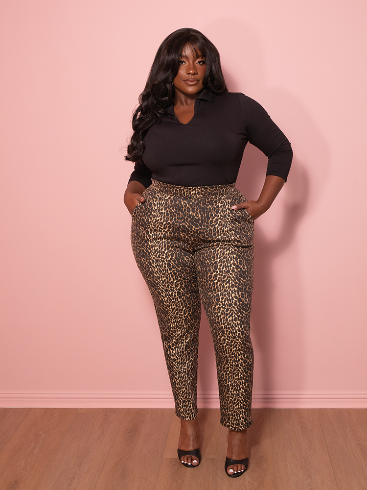 The vintage leopard print cigarette pants draped elegantly over a vintage chair, with the pink wall adding a soft contrast to the bold print.