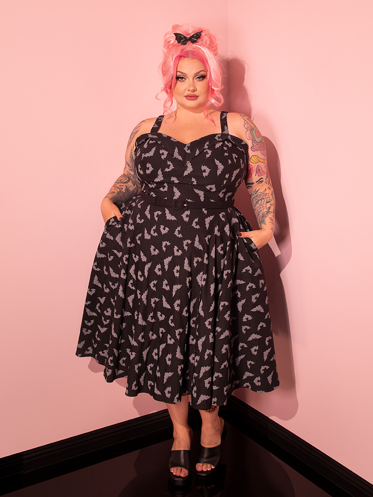 Immerse yourself in the world of vintage aesthetics as our female model dons the Maneater Swing Dress, featuring the Glow in the Dark Bat Print in Black by Vixen Clothing, the trusted retro dress brand.