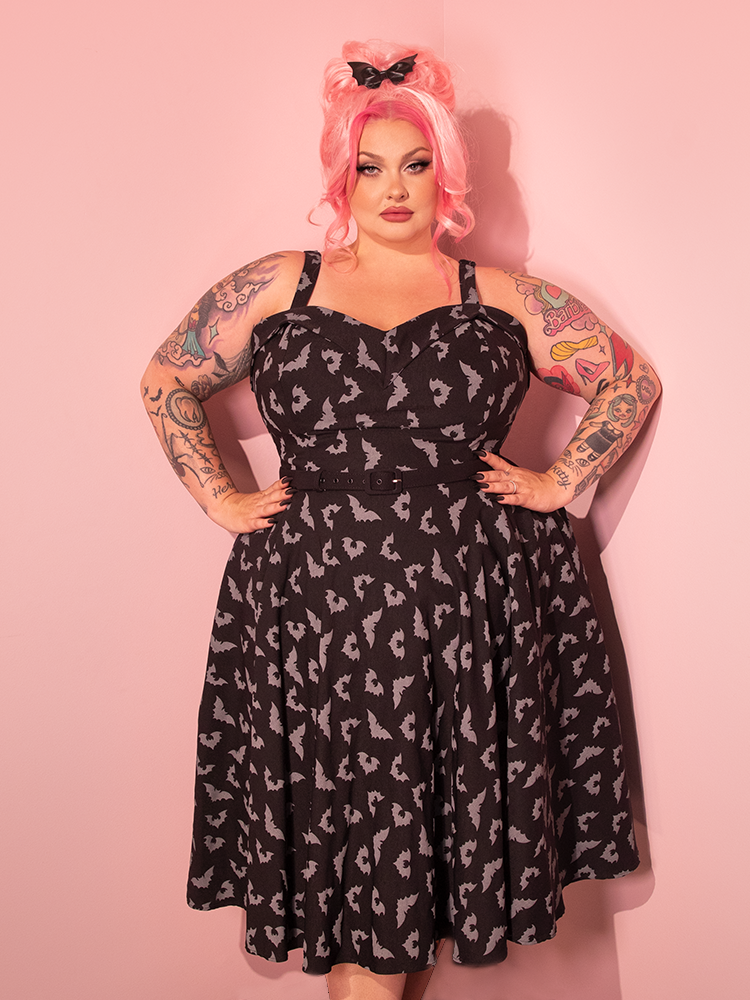 Reveal the timeless elegance of retro fashion as our gorgeous female model graces the scene in the Maneater Swing Dress, adorned with the Glow in the Dark Bat Print in Black from Vixen Clothing, the iconic retro dress brand.