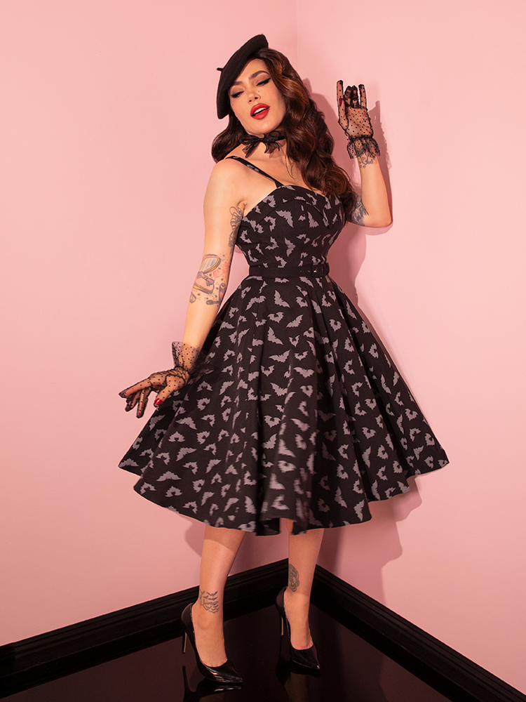 A striking brunette model showcases the Maneater Swing Dress in the Glow in the Dark Bat Print from Vixen Clothing.