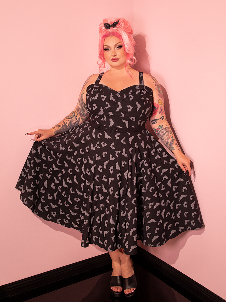 A captivating brunette model wears the Maneater Swing Dress in the Glow in the Dark Bat Print from Vixen Clothing.