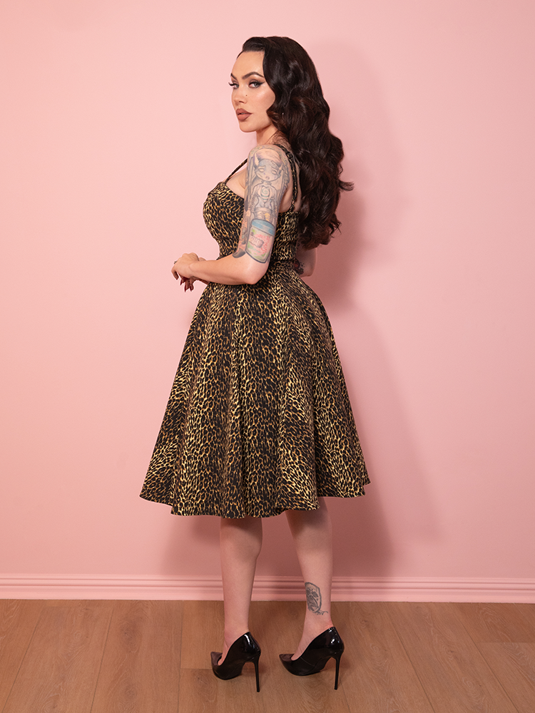 A vintage gown-inspired leopard print Maneater Swing Dress with bold flair, set against a pink wall.