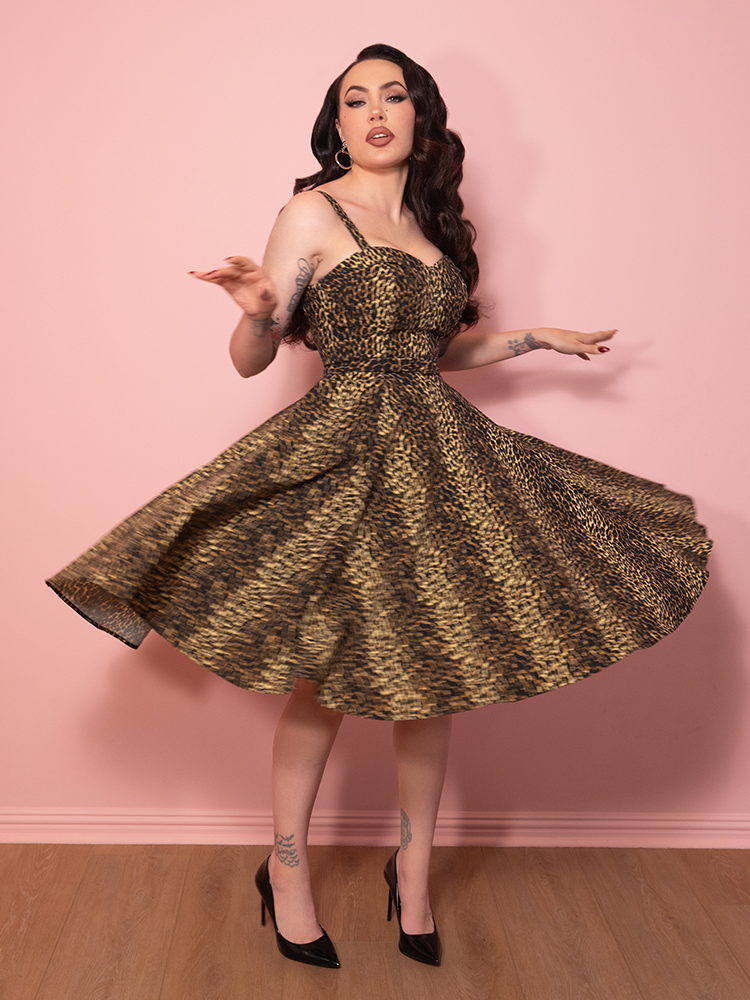 A chic vintage style leopard print Maneater Swing Dress, showcased against a pink wall for dramatic effect.