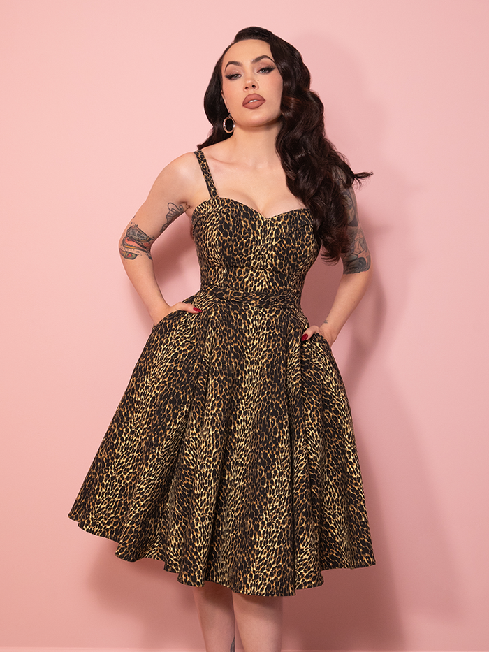 A vintage inspired Maneater Swing Dress in leopard print, styled against a pink wall with timeless glamour.