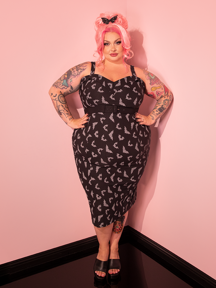 Step into the world of vintage glamour with our beautifully styled model wearing the Maneater Wiggle Dress in Black Glow in the Dark Bat Print, a masterpiece by Vixen Clothing, the go-to retro dress and clothing brand.