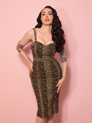 A vintage inspired Maneater Wiggle Dress in leopard print, styled against a pink wall with timeless elegance.