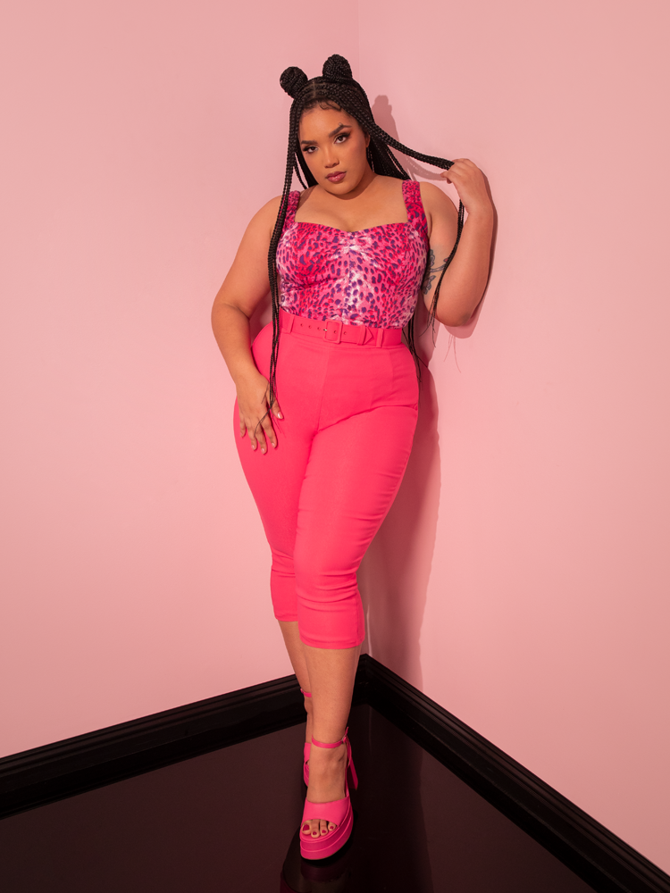 With a vintage-infused style, a breathtaking female model captivates with her pose while modeling the Pink Leopard Print Vamp Top, a captivating creation by Vixen Clothing, a renowned retro clothing brand.