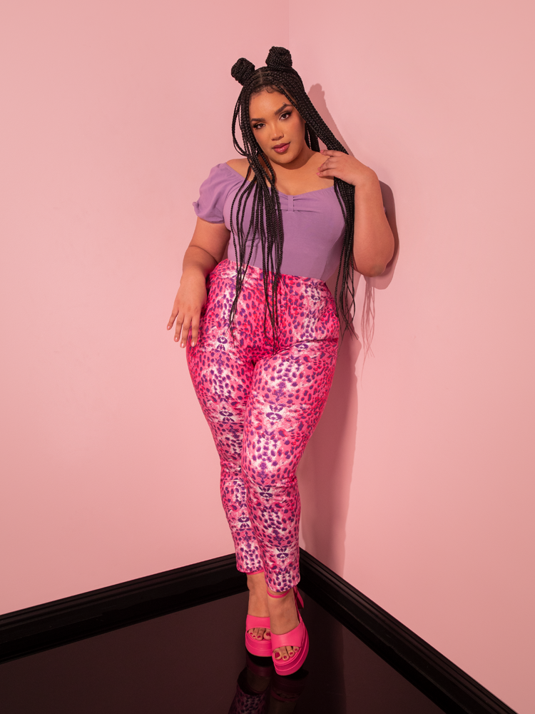 Radiating retro elegance, a captivating female model strikes a pose while wearing the Pink Leopard Print Cigarette Pants, an alluring creation by Vixen Clothing, a brand renowned for its vintage-inspired fashion.
