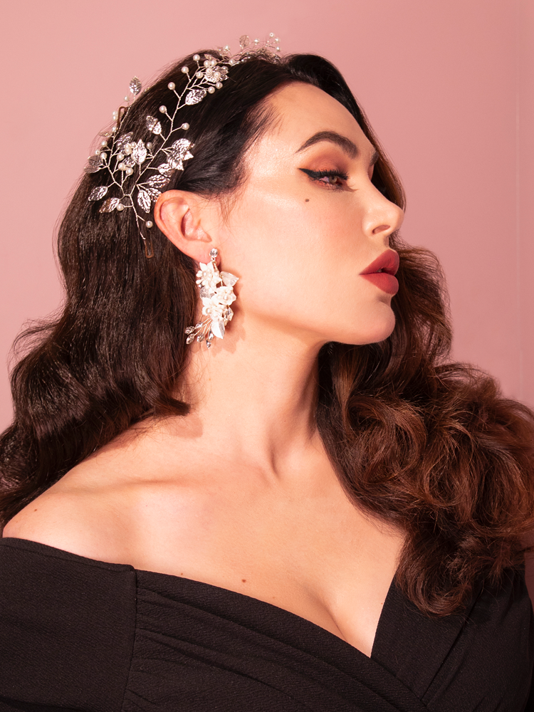 With playful flair, an attractive brunette model strikes a pose wearing the Vintage-Style Leaf and Pearl Hair Wire in Silver from the retro clothing brand Vixen Clothing.
