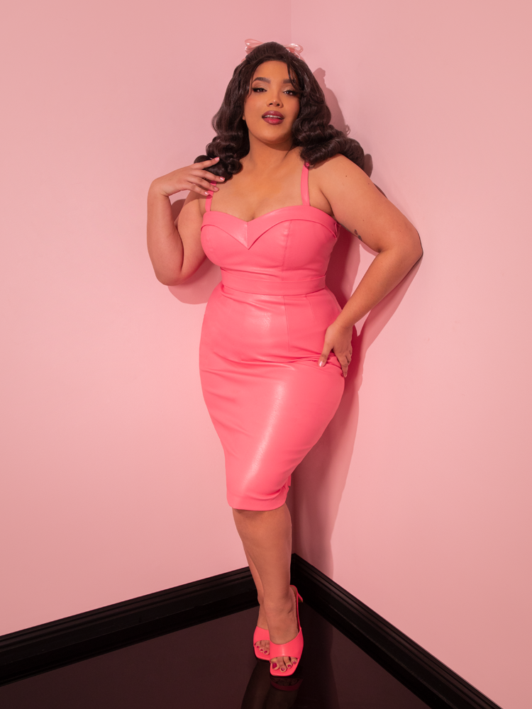 Let the glamorous aura of the stunning model mesmerize you as she dons the all new Bad Girl Maneater Top, a stunning creation in Flamingo Pink Vegan Leather from Vixen Clothing, a brand known for its unrivaled expertise in retro and vintage wear.