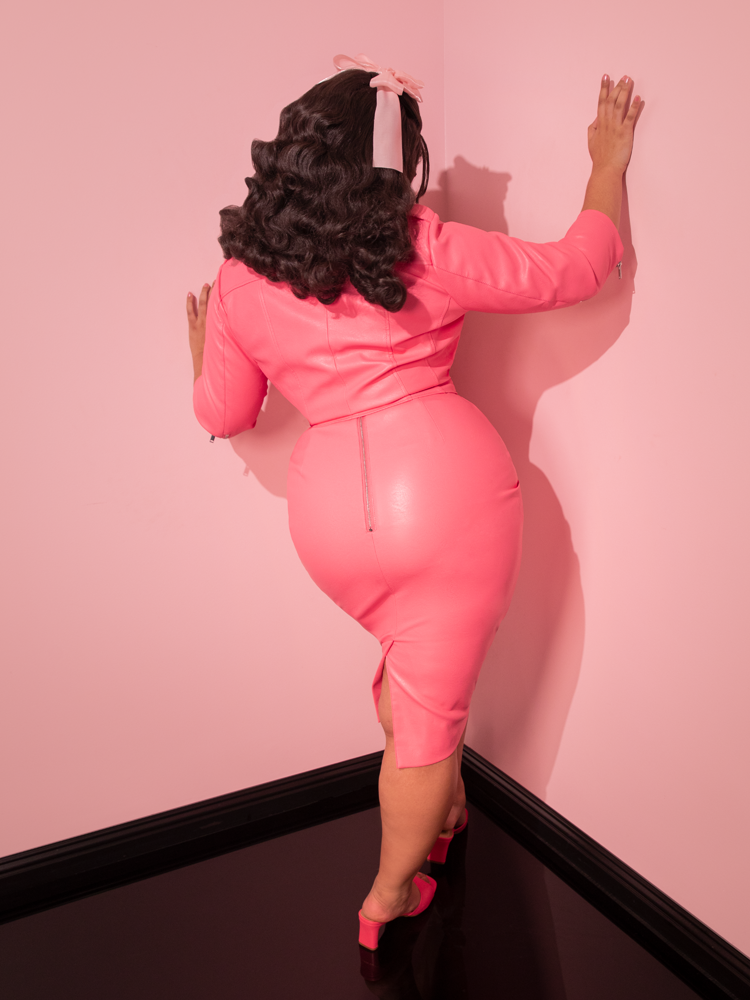 The nostalgic elegance of the retro era is brought to life by the stunning dame, radiating charm in the Bad Girl Pencil Skirt in Flamingo Pink Vegan Leather from Vixen Clothing, a cherished vintage dress brand.