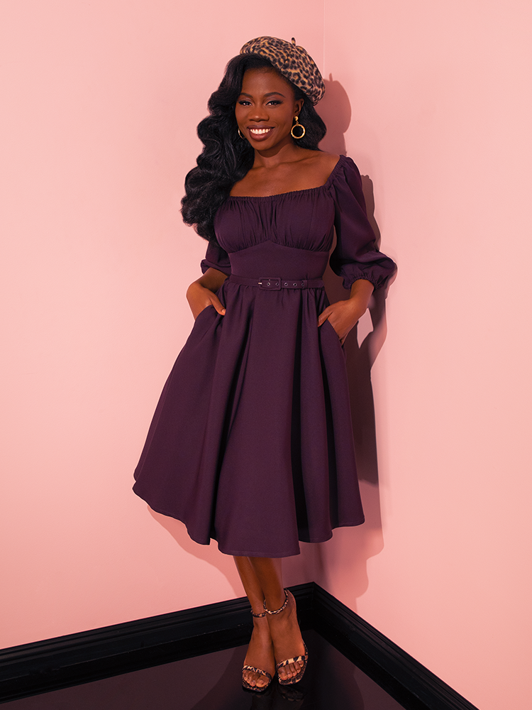 With a mix of fun and flirtiness, female models showcase the Vacation Dress in Plum from Vixen Clothing, embodying the brand's dedication to creating lively retro clothing.