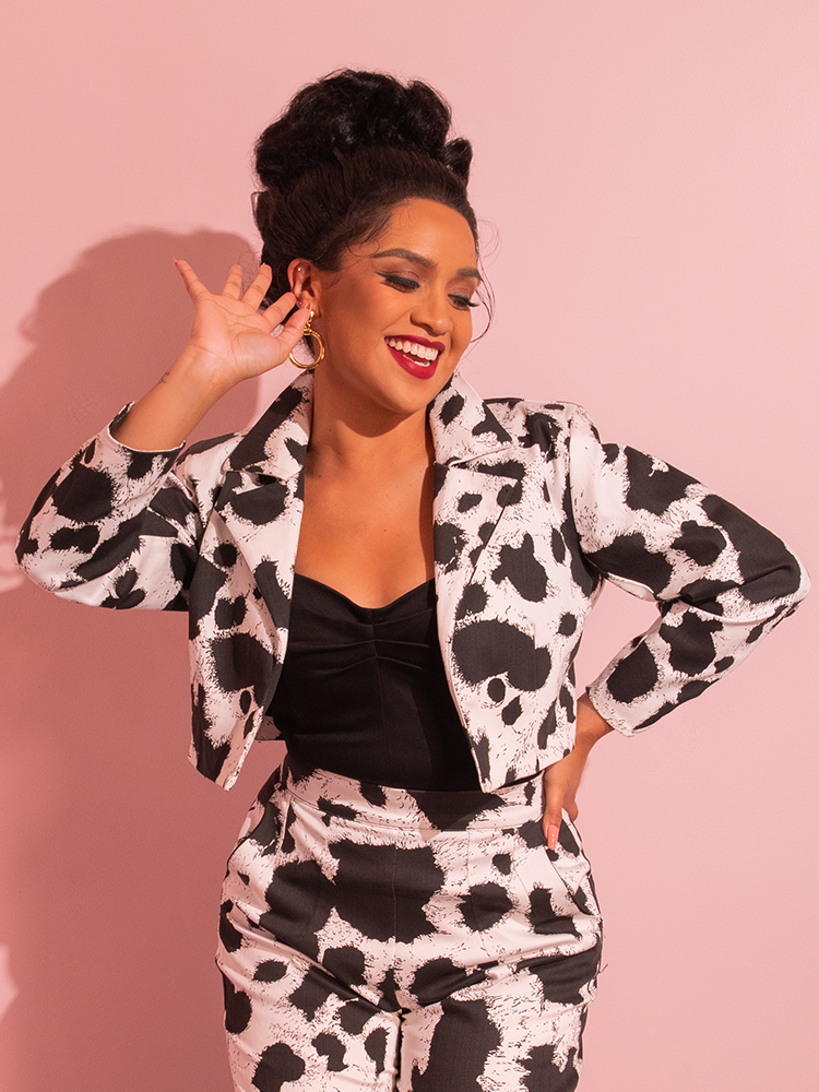 In a captivating display, a gorgeous female model exudes timeless charm while wearing the Rebel Cropped Jacket in Cow Print by Vixen Clothing, a brand known for its retro-inspired creations.