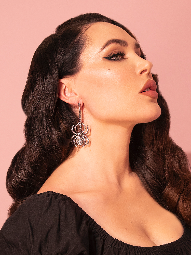 With the Rhinestone Spider Dangle Earrings in Silver by Vixen Clothing, Micheline Pitt exudes a timeless retro elegance.