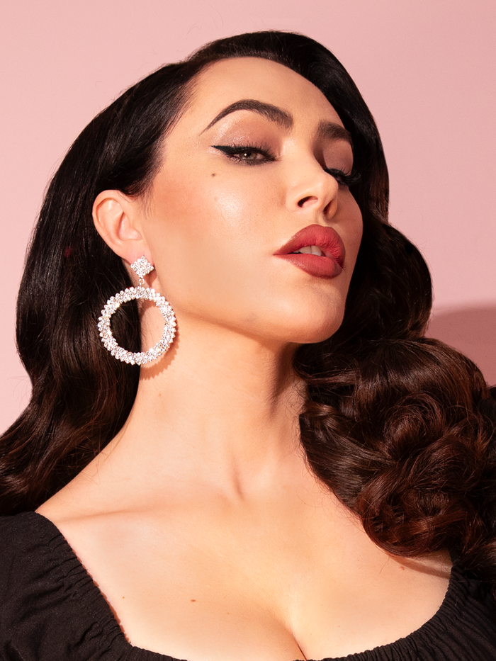 Micheline Pitt models the Rhinestone Hoop Earrings in Silver from retro clothing brand Vixen Clothing.