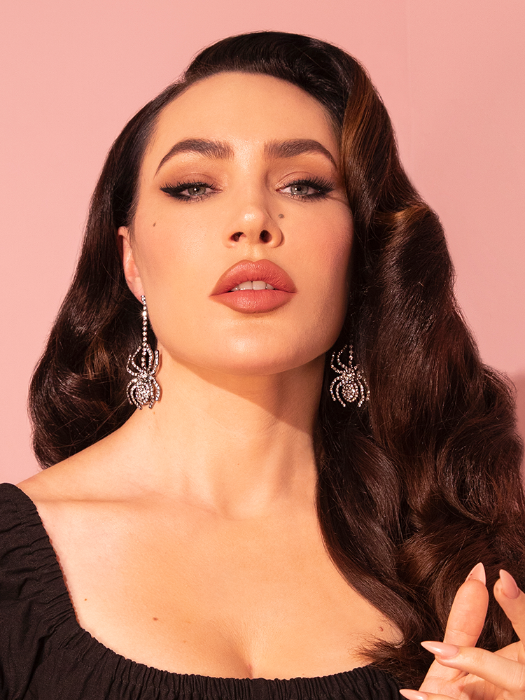 Donning a pair of Silver Rhinestone Spider Dangle Earrings from the retro fashion purveyor Vixen Clothing, Micheline Pitt epitomizes retro allure.