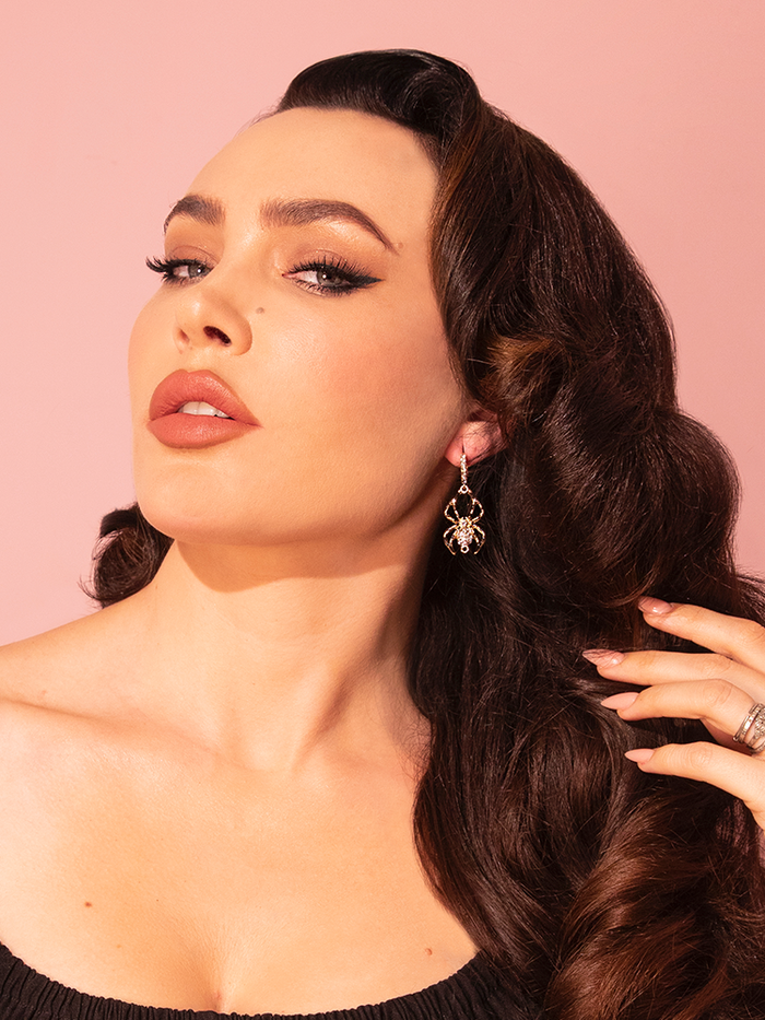A stunning brunette model showcases the Rhinestone Black Widow Hoop Earrings in Black by the vintage fashion label Vixen Clothing.