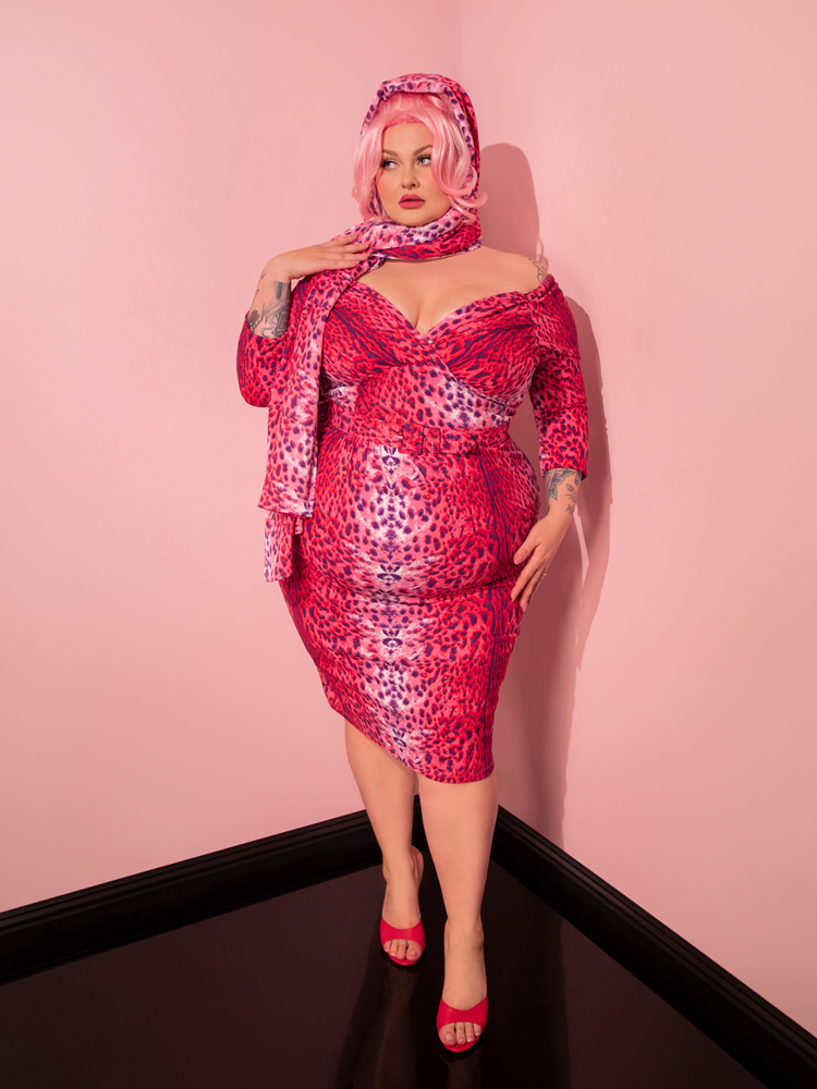 Behold the breathtaking beauty of a female model, radiating retro charm while donning the Pink Leopard Print Starlet Wiggle Dress and Scarf from the renowned Vixen Clothing.