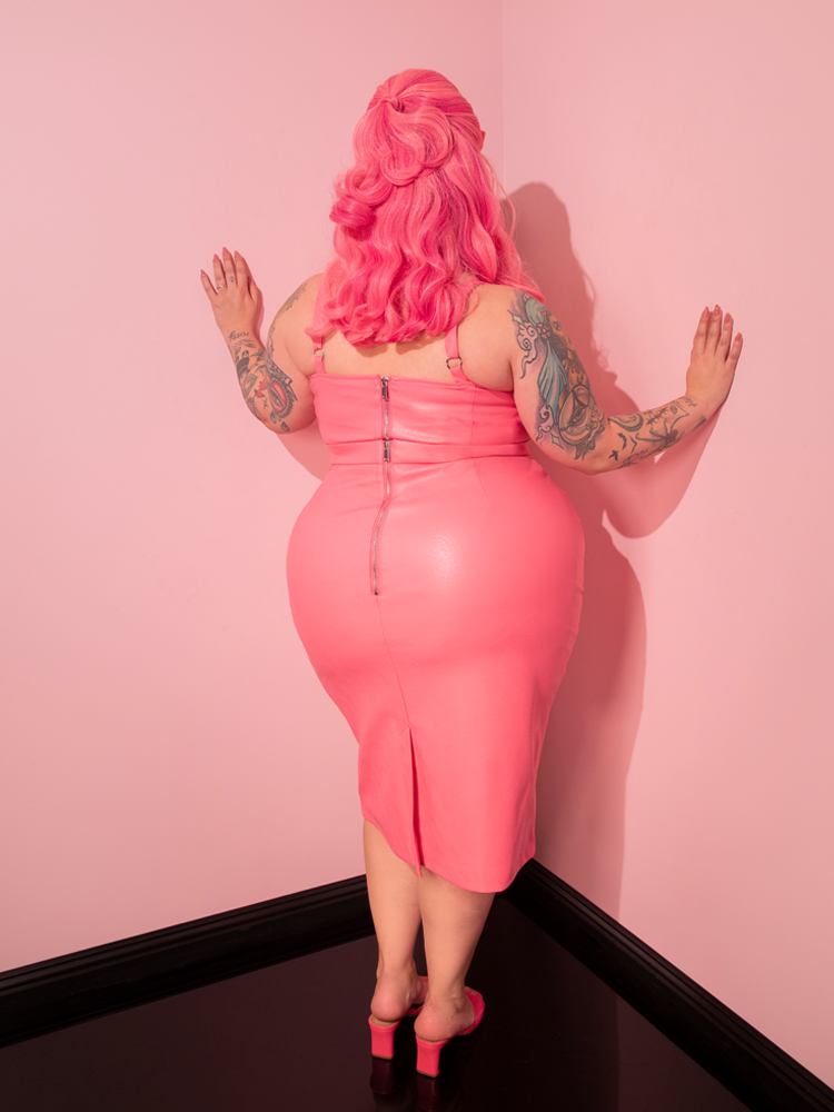 Marvel at the mesmerizing vision of the beautiful woman, showcasing the Bad Girl Pencil Skirt in Flamingo Pink Vegan Leather from Vixen Clothing, a brand known for its exceptional retro and vintage designs.